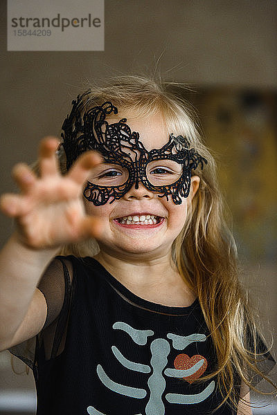 Kleines lächelndes Mädchen in Maske zu Halloween in Skelettkostüm gekleidet