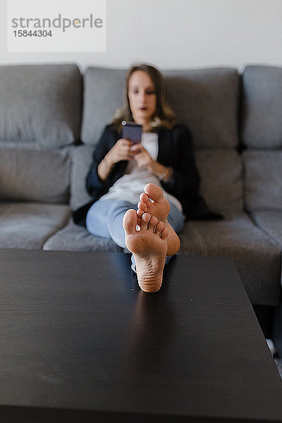 Frau auf einer Couch mit unfokussiertem Mobiltelefon