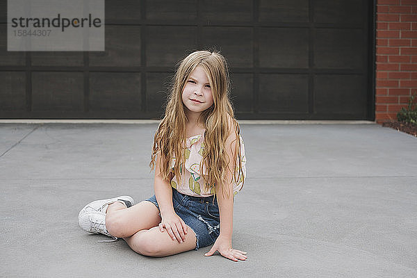Porträt eines süßen jungen Mädchens  das vor einem Garagentor sitzt