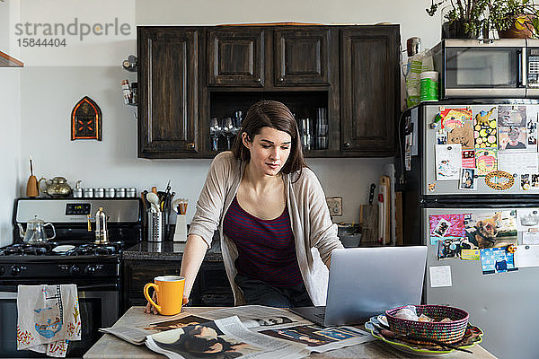 Junge Frau benutzt Laptop  während sie in der Küche Kaffee am Tisch trinkt