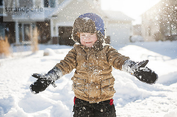 Kleinkind spielt und lächelt beim Schneewerfen vor dem Haus