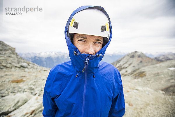 Porträt eines Bergsteigers mit Helm und Regenjacke.