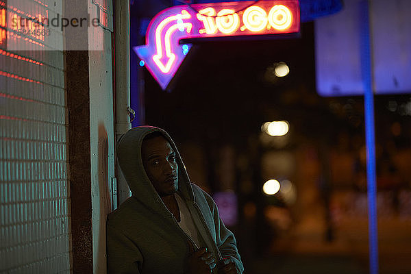 Afroamerikanischer Mann mit Kapuzenpulli unter Neonreklame in der Nacht
