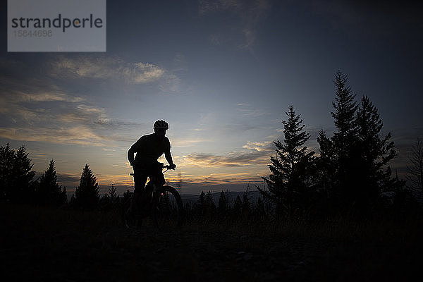 Ein Mountainbiker als Silhouette bei Sonnenuntergang auf dem Gipfel des Blue Mountain.