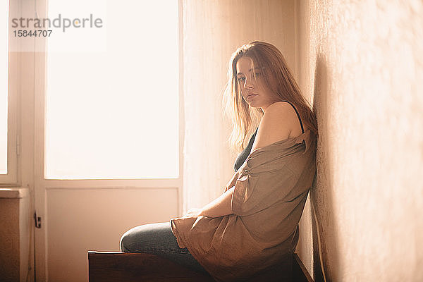 Porträt einer jungen Frau  die zu Hause am Kopfende des Bettes am Fenster sitzt