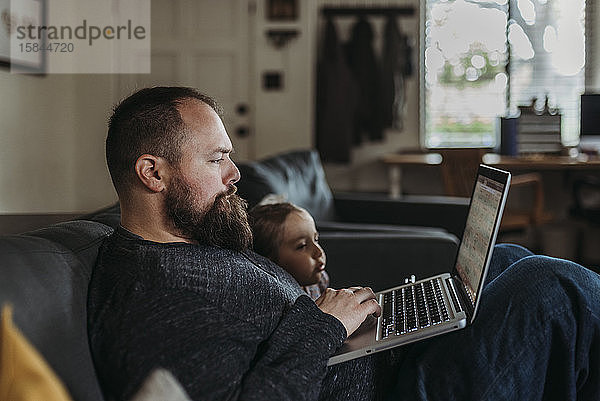 Nahaufnahme eines Vaters  der mit seiner kleinen Tochter von zu Hause aus arbeitet