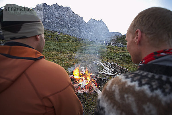 2 männliche Freunde sitzen an einem Lagerfeuer in Grönland