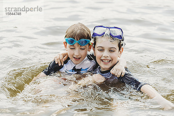 Zwei Brüder mit Schwimmbrille umarmen sich im Wasser