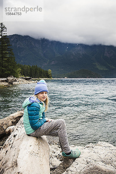 Junges Mädchen sitzt auf Baumstamm gegen See und Berge