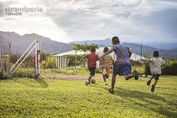 Eine Gruppe von Freunden spielt vor Sonnenuntergang auf einem Rasenplatz Fußball.