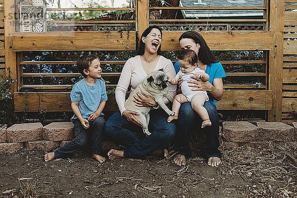 Baby berührender Mops mit lachender barfüssiger Zwei-Mütter-Familie