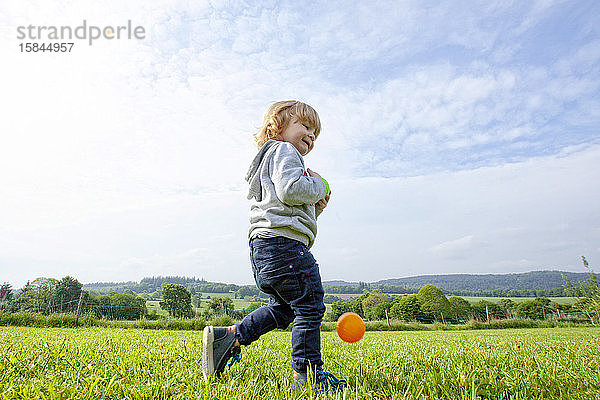 ein kleiner Junge  der auf einer grünen Wiese auf dem Land Bälle spielt und Spaß hat  Caurel Bretagne  Frankreich.