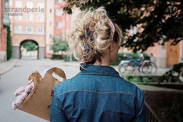 der Rücken einer blonden Frau  die einen Blumenstrauss auf der Strasse hält