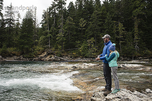 Vater und Tochter stehen auf Felsen und fischen an einem Fluss