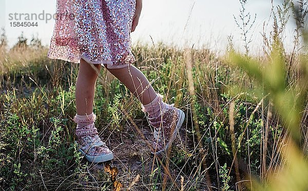 junge Mädchen mit funkelnden Schuhen und Kleidern in der Mitte eines Feldes bei Sonnenuntergang