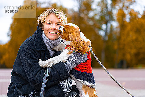 Frau lächelt im Park mit einem Cavalier King Charles Spaniel Hund.