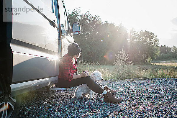 Frau  die Kaffee trinkt  während sie mit ihrem Hund in einem Wohnmobil zeltet