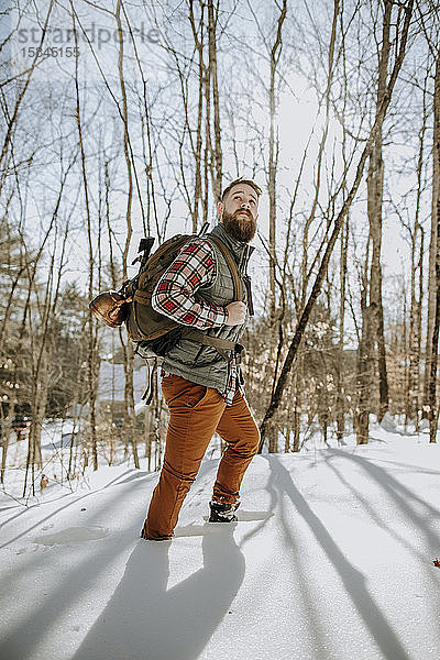 Mann mit Bart in Flanellwäsche wandert durch Schnee in den Wäldern von Maine