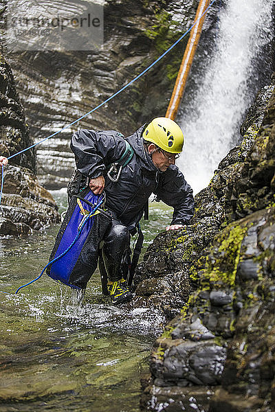 Abenteuerlustiger Mann steigt aus dem Fluss  nachdem er sich an einem Wasserfall abgeseilt hat.