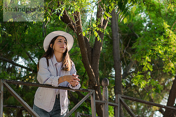 Junge Frau mit Hut steht auf einer Parkbrücke. Abenteuer  Tourismus.