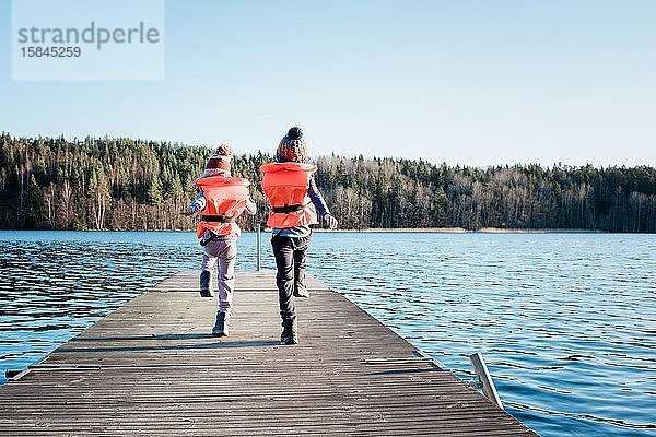 Geschwister marschieren am Strand am Pier entlang und spielen