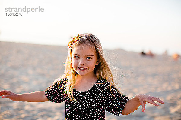 Junges Mädchen spielt am Strand und lächelt bei Sonnenuntergang in die Kamera