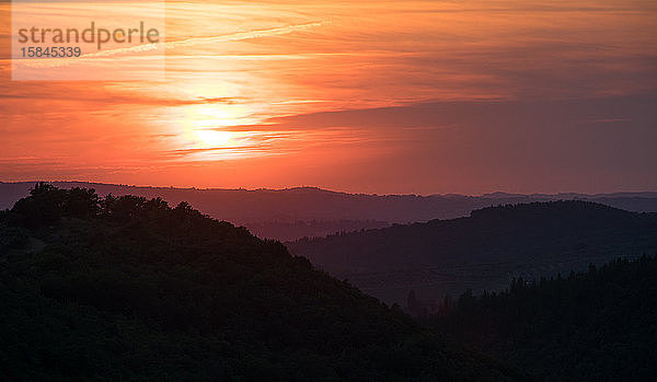 Erstaunlicher Sonnenaufgang oder Sonnenuntergang in den Bergen der Toskana  Italien. Die orangefarbene Sonne scheint über die grauen Wolken und beleuchtet die dunklen Täler und Berge. Horizontale Aufnahme