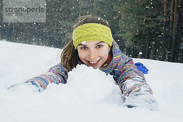 Mädchen liegt im Schnee und lächelt