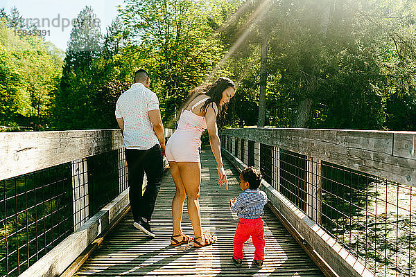 Blick von hinten auf eine Familie  die auf einer Brücke mit Sonneneruption geht