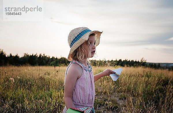Porträt eines jungen Mädchens  das auf einer Wiese mit Papierflugzeugen spielt