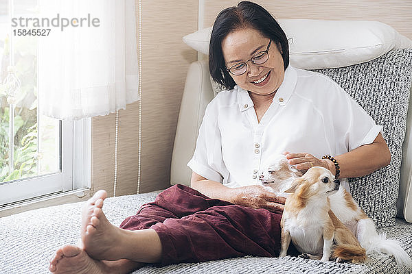 Glückliche ältere Frau mit ihren Hunden auf der Couch in ihrem Haus.