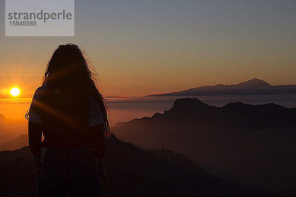 Frau mit langem Gehör  die den Sonnenuntergang betrachtet  während sie auf einem Berg steht