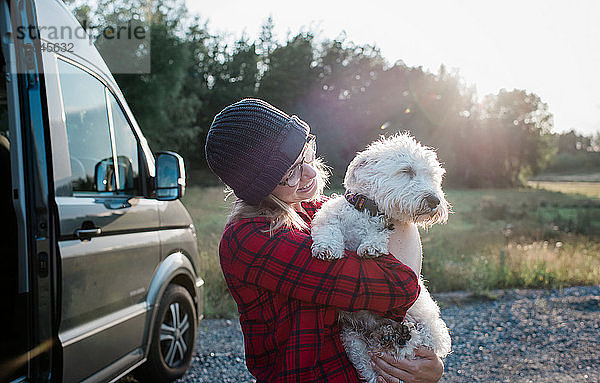 Porträt einer Frau  die beim Camping ihren Hund lächelnd und glücklich aussehend hält