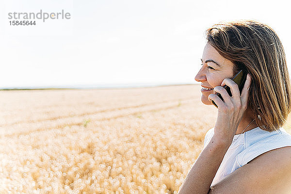 Hübsche Frau bei einem Telefongespräch auf dem goldenen Feld