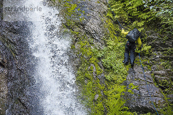 Backpacker seilt sich neben einem rauschenden Wasserfall ab.