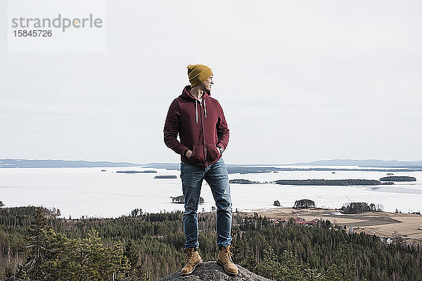 Mann  der auf einem Felsen steht  während er einen Hügel über dem Meer in Schweden wandert