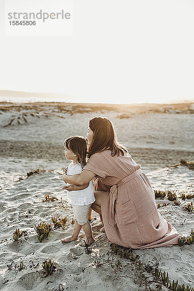 Seitlicher Virew der Mutter umarmt Kleinkindzwillinge am Strand