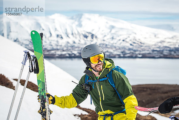 Ein Mann mit Skiausrüstung und Bergen und Wasser im Rücken