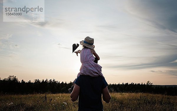 Vater trägt seine Tochter bei Sonnenuntergang auf den Schultern auf einer Wiese