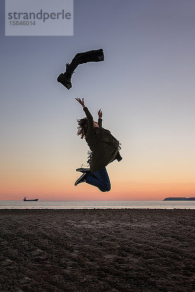 Junge Frau springt bei Sonnenuntergang an den Strand. Lebensstil  Freiheit