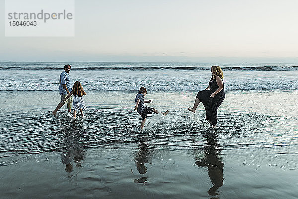 Vierköpfige Familie  die in der Abenddämmerung im Meer spielen und sich gegenseitig bespritzen