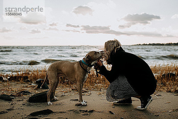 Frau  die im Winter ihren Hund am Strand küsst