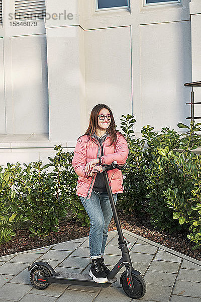 ein tausendjähriges junges Mädchen in einer rosa Jacke auf einem Elektroroller