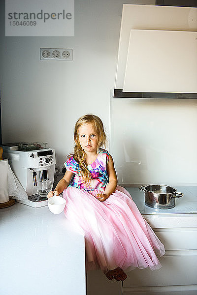 Kleines Mädchen in einem schönen Kleid  das auf dem Küchentisch sitzt
