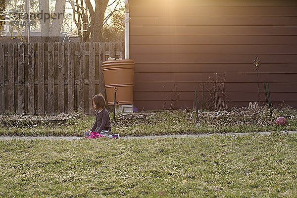Ein fokussiertes kleines Mädchen sitzt bei Sonnenuntergang auf einem Pfad im Hof und schreibt einen Brief