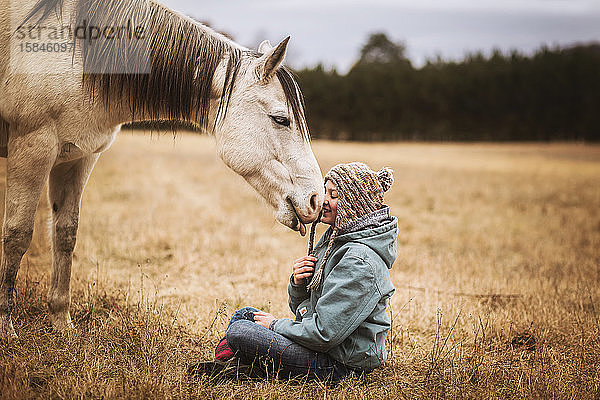Fröhliches Pferdelecken junger Mädchen auf einem Feld im Herbst
