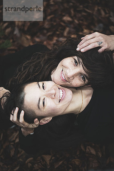 Glückliches lesbisches Paar lächelt in die Kamera  als sie in goldenem Waldblatt liegen