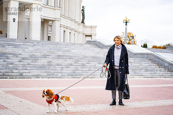 Eine Frau geht mit einem Cavalier King Charles Spaniel Hund durch die Stadt.