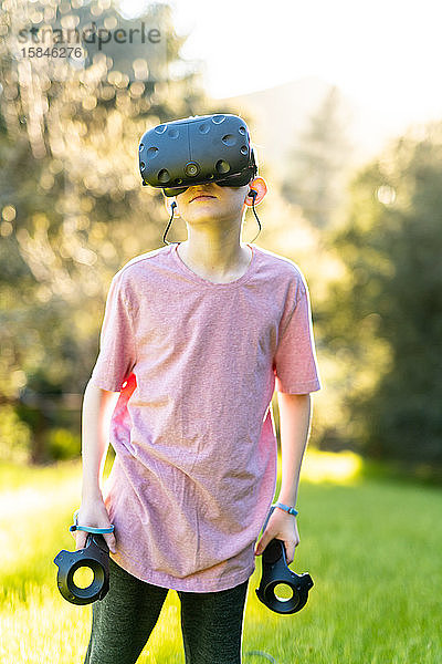 Junge steht mit eingeschalteter VR-Technologie im Freien an einem sonnigen Tag