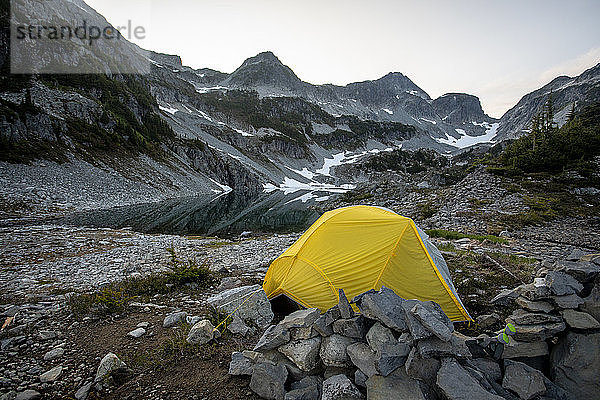 Ein Zelt wird neben einem Alpensee und Bergen aufgestellt.